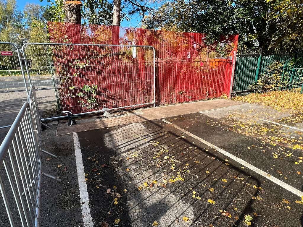 Temporary fencing and barriers at a construction site with fallen leaves on the ground.