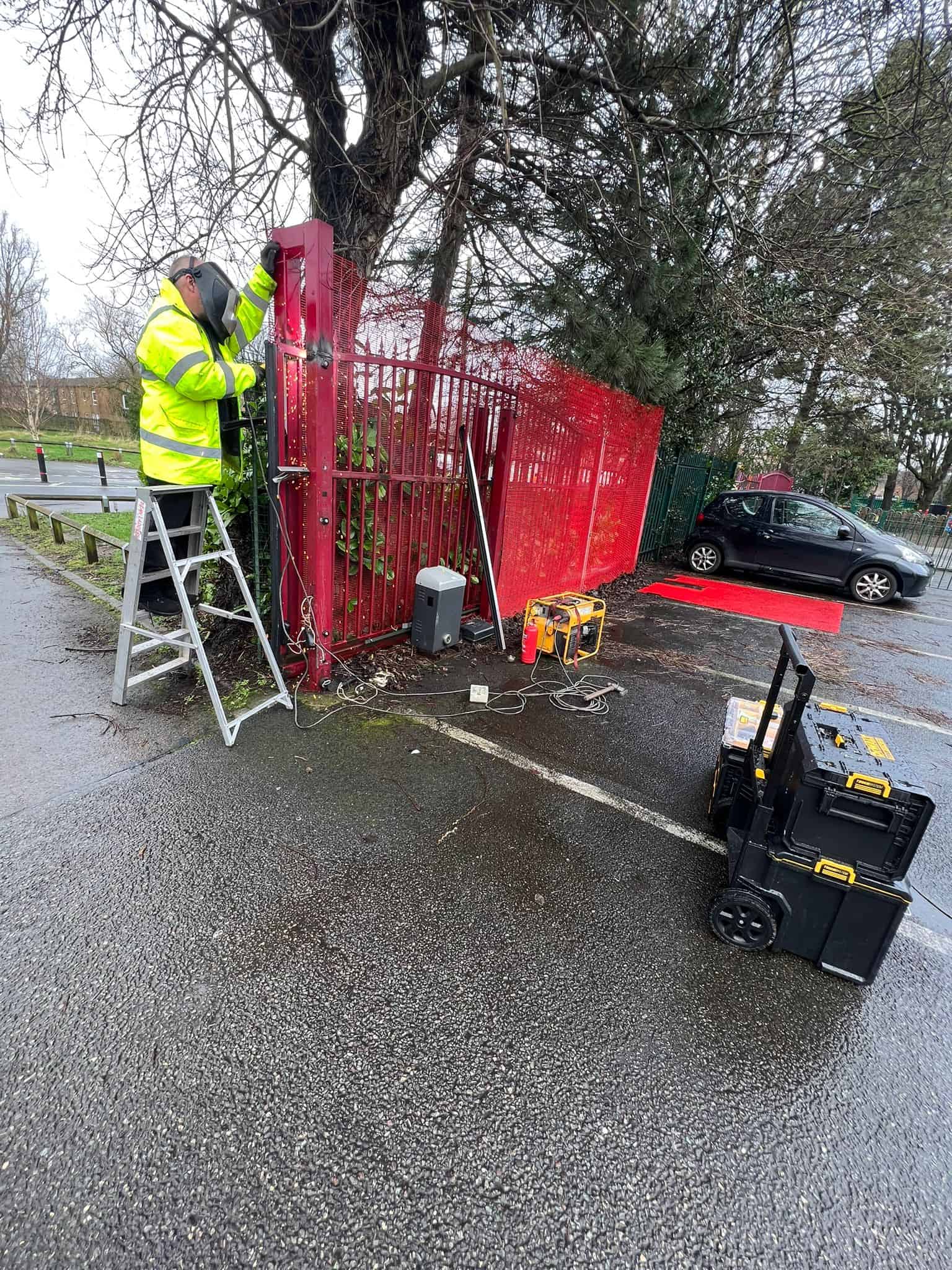 Alarm system installation being carried out by a technician in high-visibility clothing at a red gat.