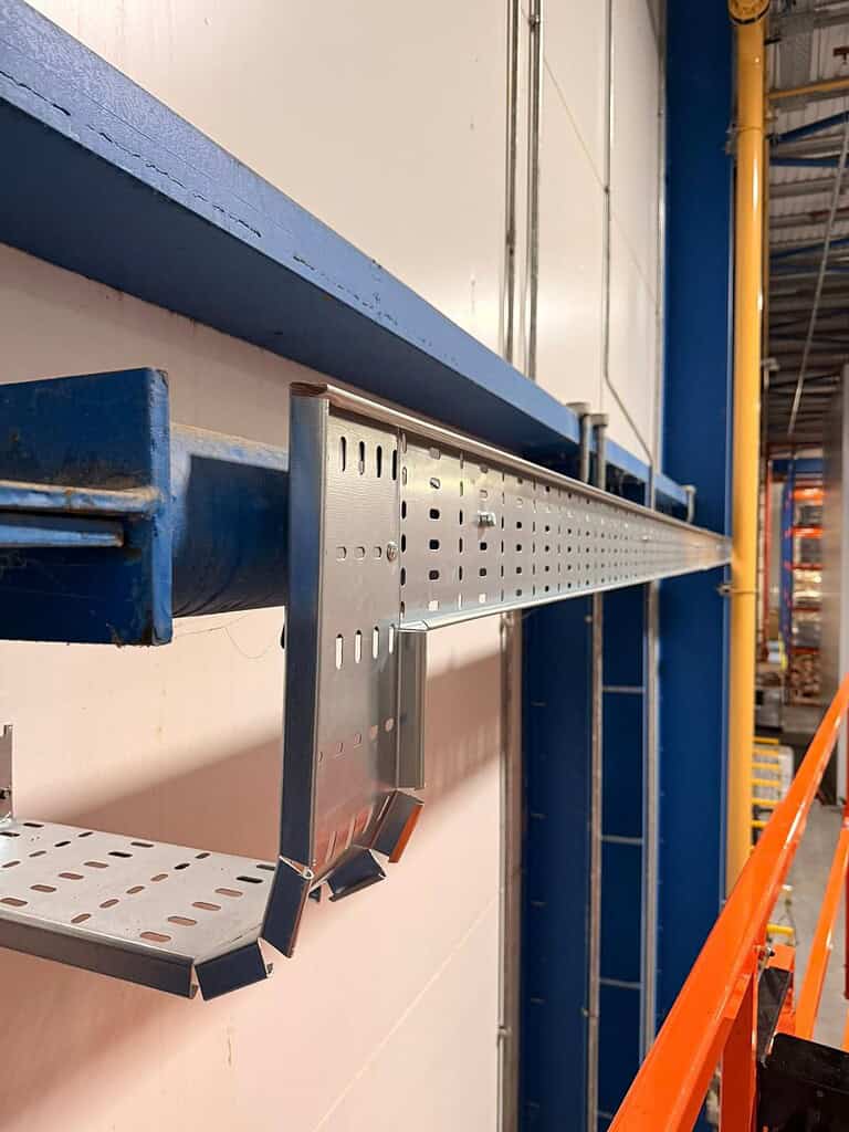 Industrial cable management system with perforated metal cable tray in warehouse.